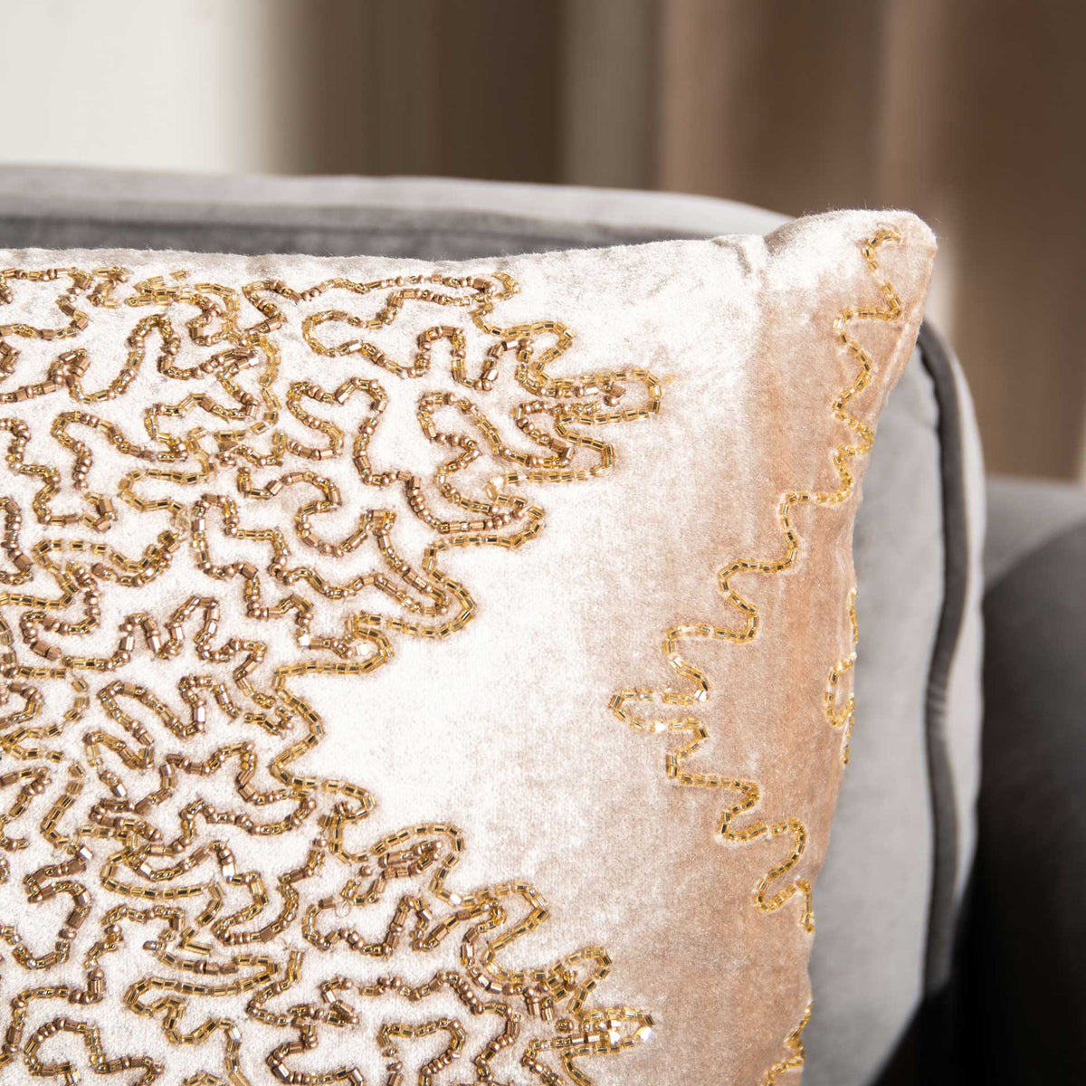 Intricate gold beadwork adds shimmering texture to the pillow's soft beige fabric.