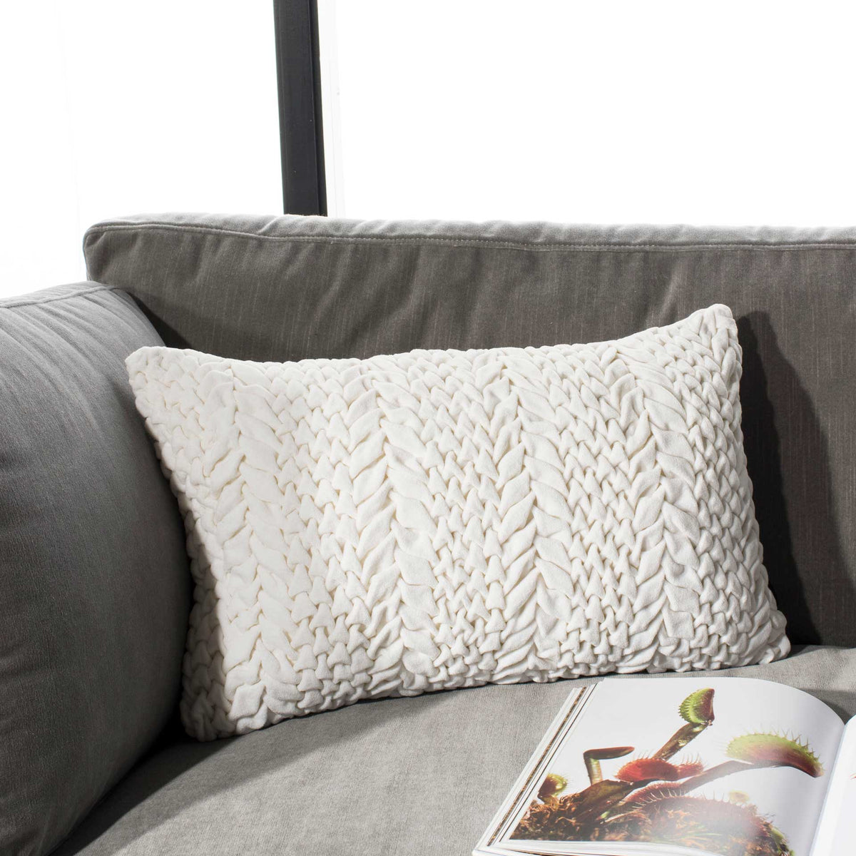 Cream lumbar pillow adds dimensional, gathered texture to a gray sofa