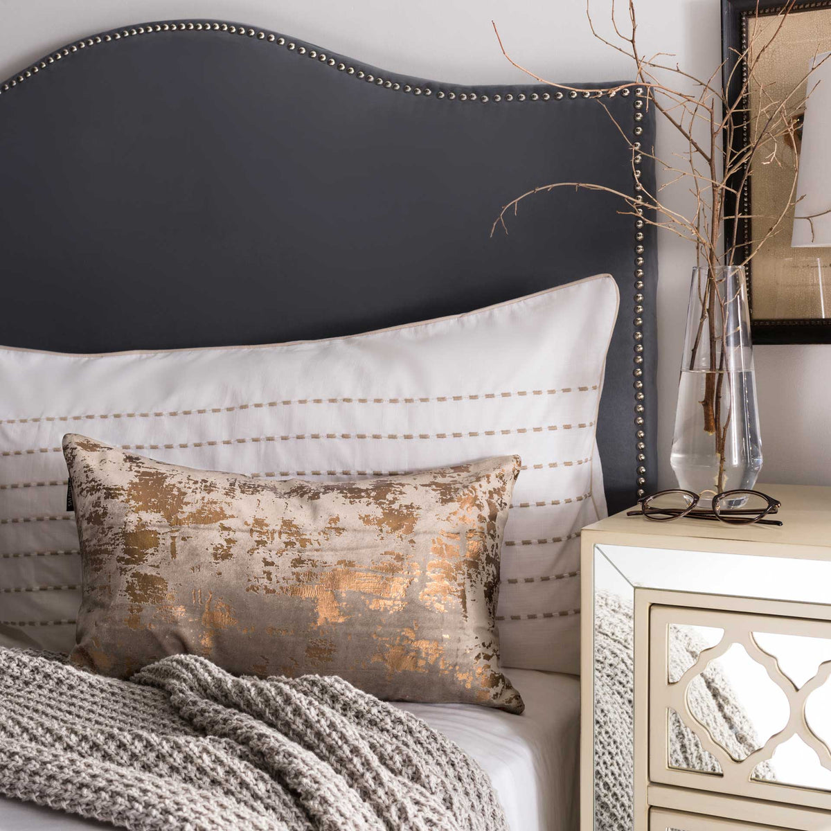 Brown and copper lumbar pillow adds a warm metallic accent to layered bedding.