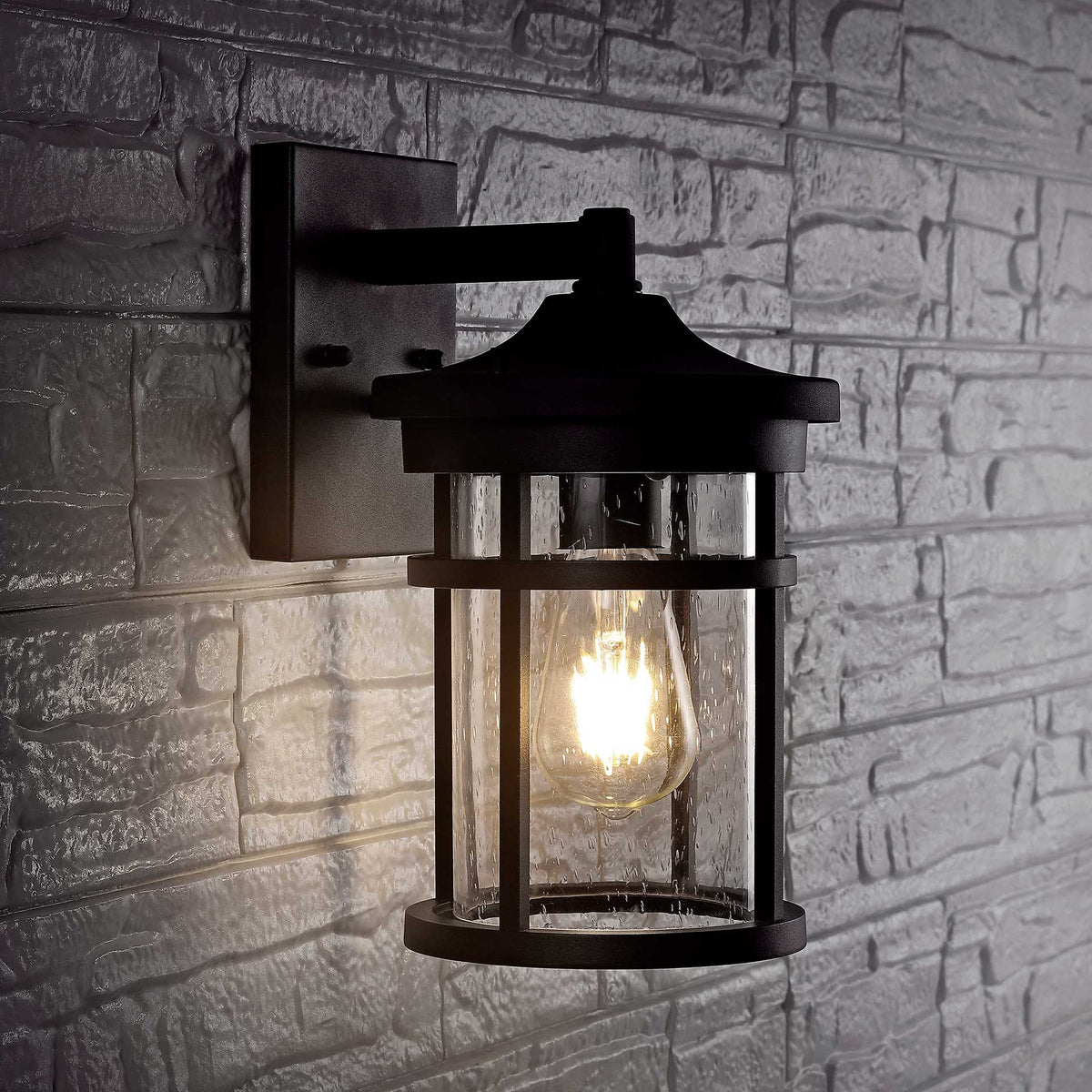 Black metal wall lantern casts a warm glow across a textured stone wall