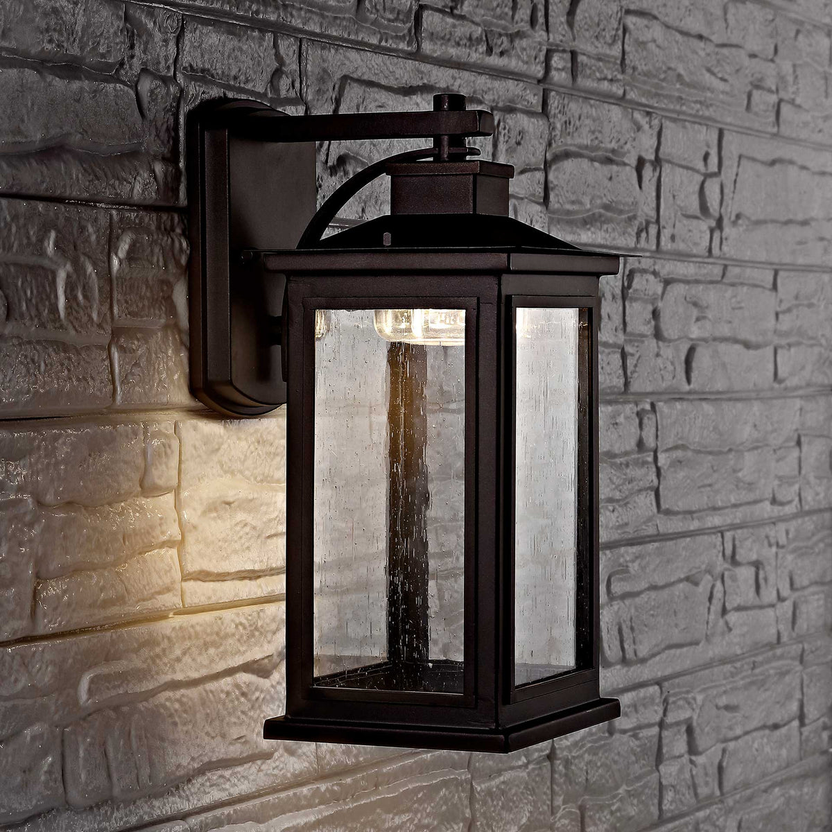 A bronze wall lantern casts a warm glow across a textured stone wall