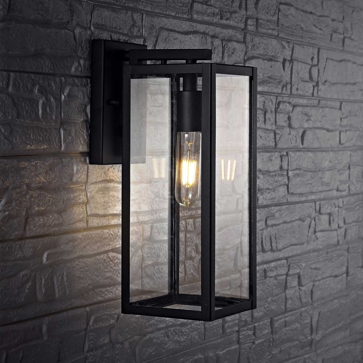 Black metal wall lantern casts a warm glow against a dark, textured stone wall