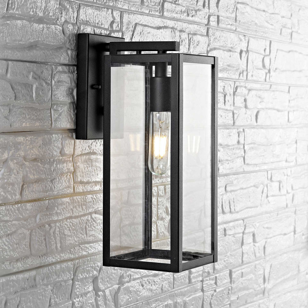 Tall glass wall lantern with a glowing tubular bulb brightens a pale stone wall