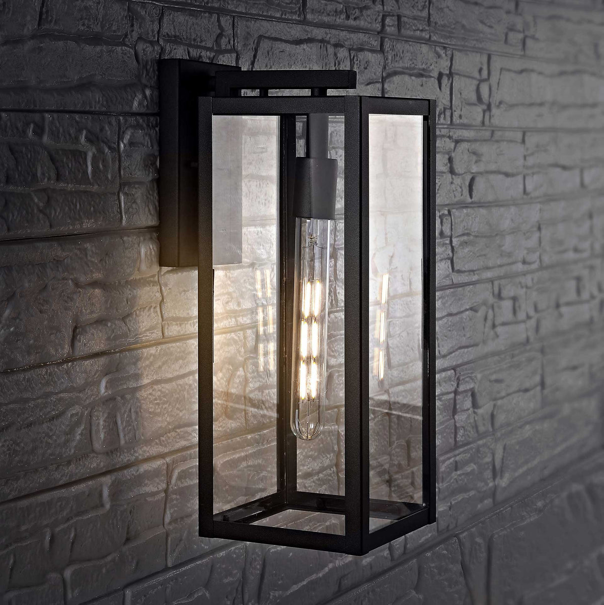 Clear glass outdoor wall lantern casts a warm glow against dark textured brick