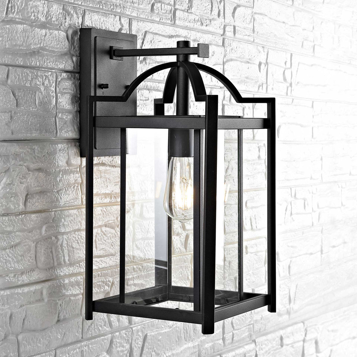 Rectangular black wall lantern with a curved arm and clear glass panels illuminates a stone wall