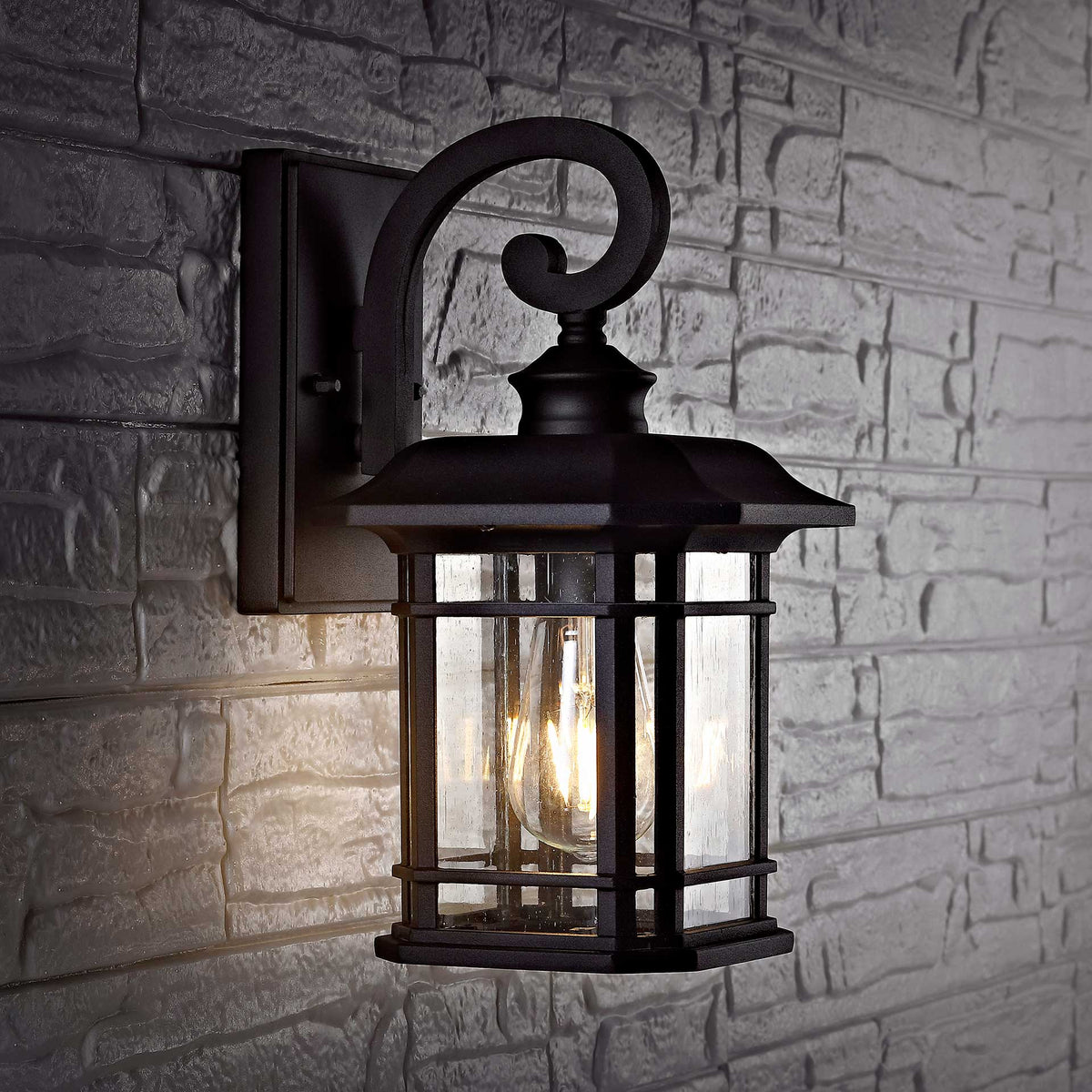 Warm light shines through the glass of a black wall lantern against textured brick.