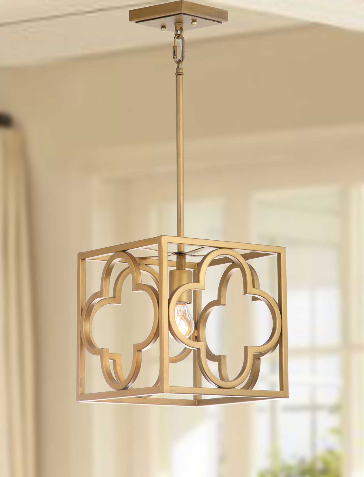 Warm light glows within the gold pendant's sculptural quatrefoil frame.