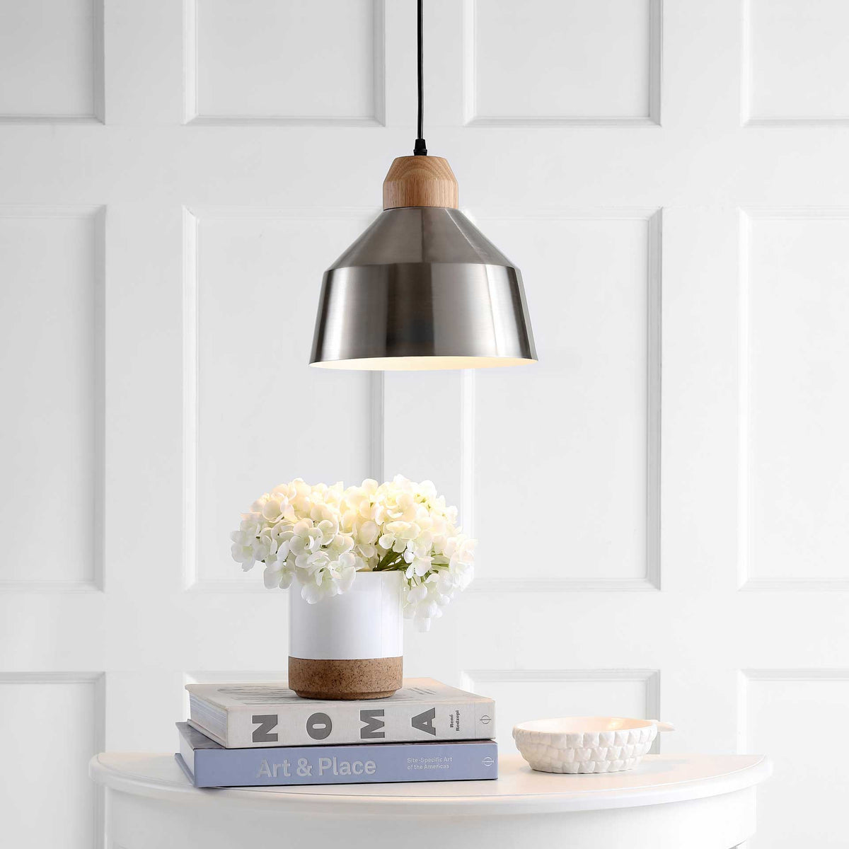 A warm downlight glows beneath the silver-toned shade and pale wood detail