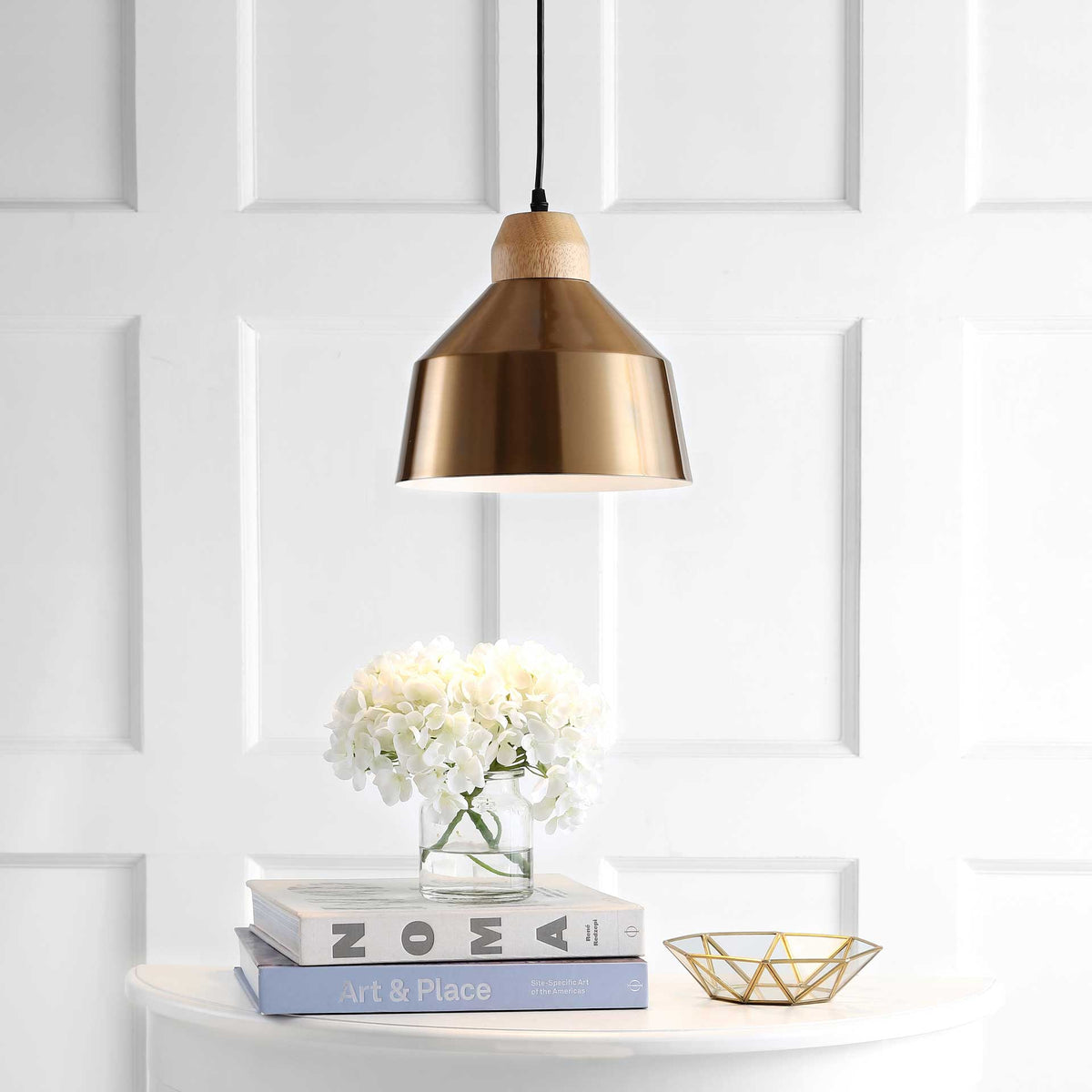 The gold pendant casts a soft downlight from its flared shade and pale wood accent