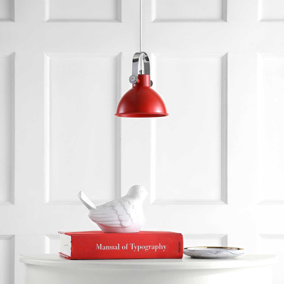A vivid red dome pendant adds color above a white table with a red book and bird accent