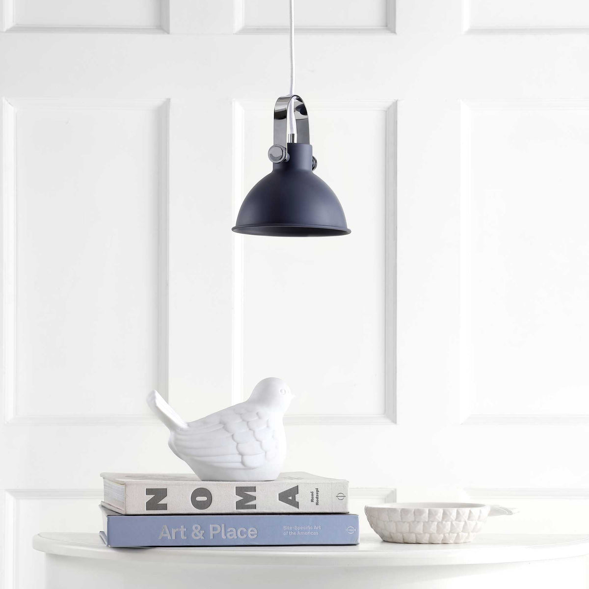 Charcoal dome pendant adds a sleek accent above a white table with books and sculptural decor