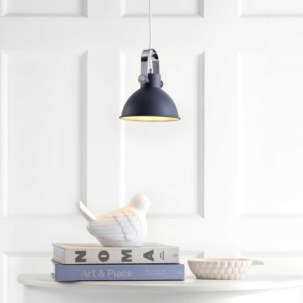 A dark gray dome casts a warm glow over a white tabletop and decorative bird