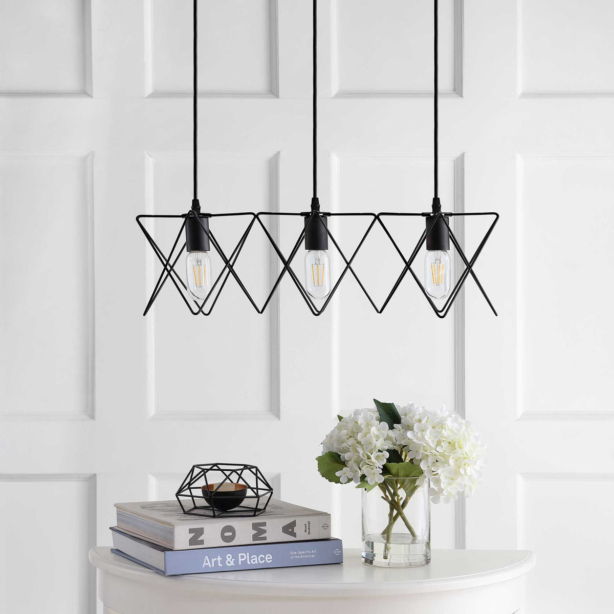 Three clear bulbs hang within open black wire shades above a white table
