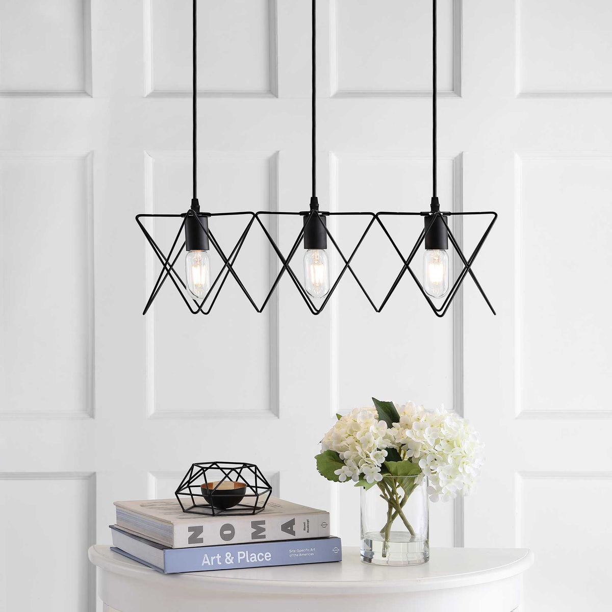 Soft light glows from three bulbs framed by geometric black wire shades
