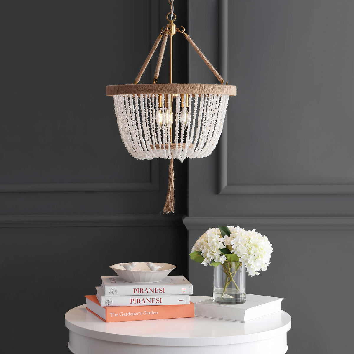A warm glow filters through white bead strands, highlighting the rope-wrapped rim and tassel