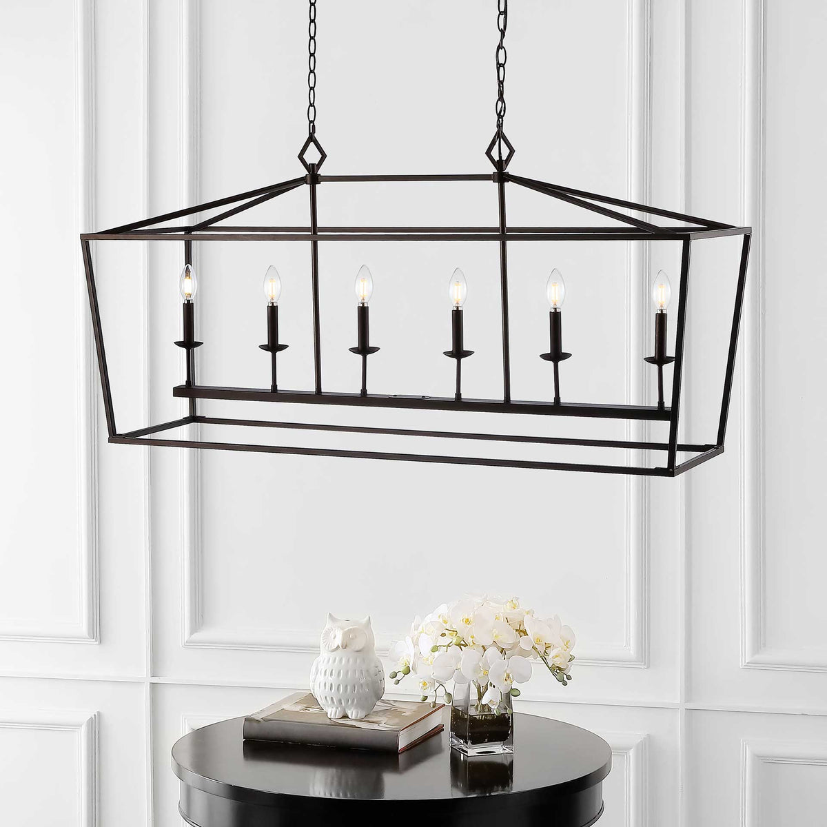 Six lit candle-style bulbs brighten the open bronze frame above a round table
