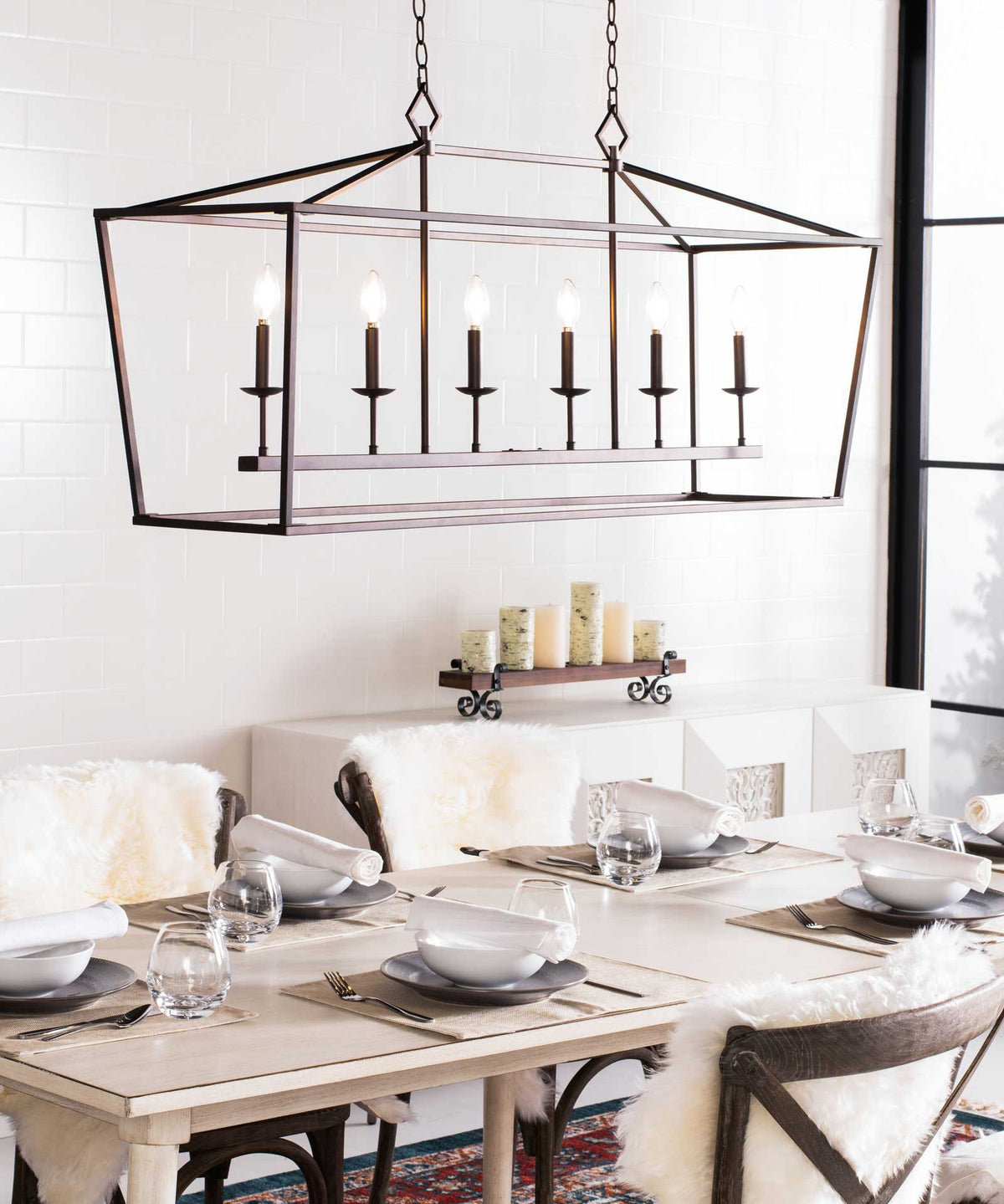 A wide, open-frame bronze pendant brings six glowing candle lights above a dining table