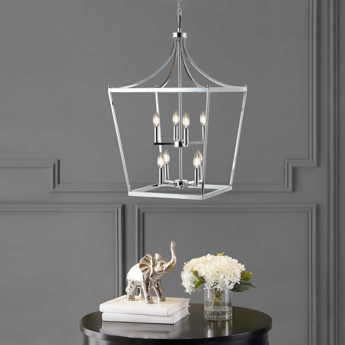 A tiered cluster of glowing bulbs lights up the chrome lantern pendant over a dark round table.