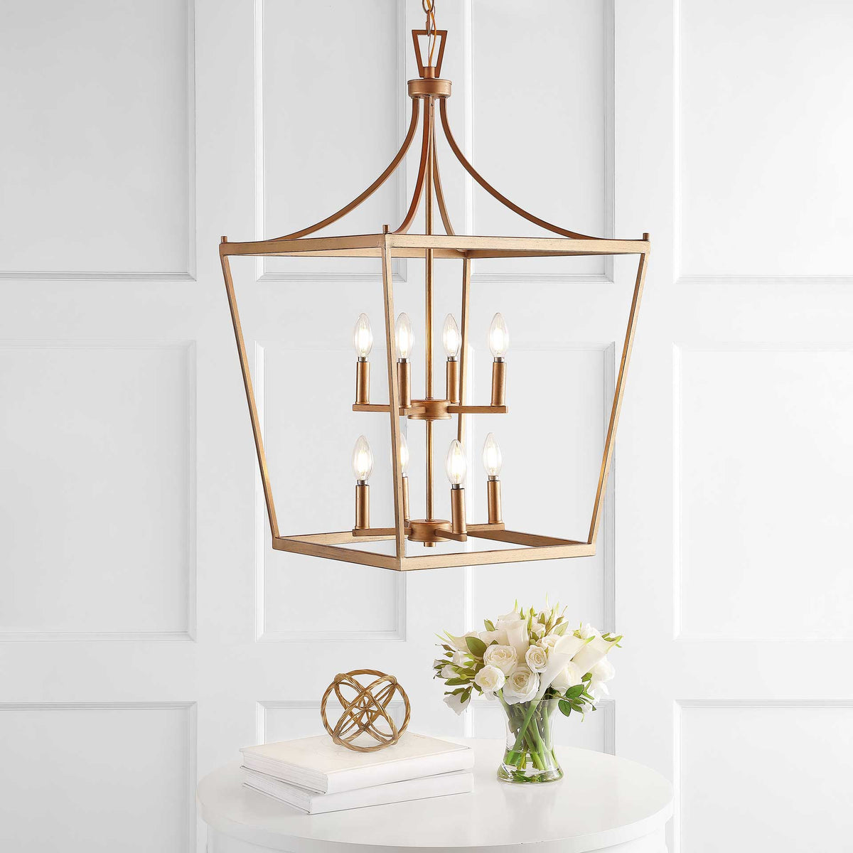 Warm light from eight candle bulbs glows within the open gold frame above a white accent table.