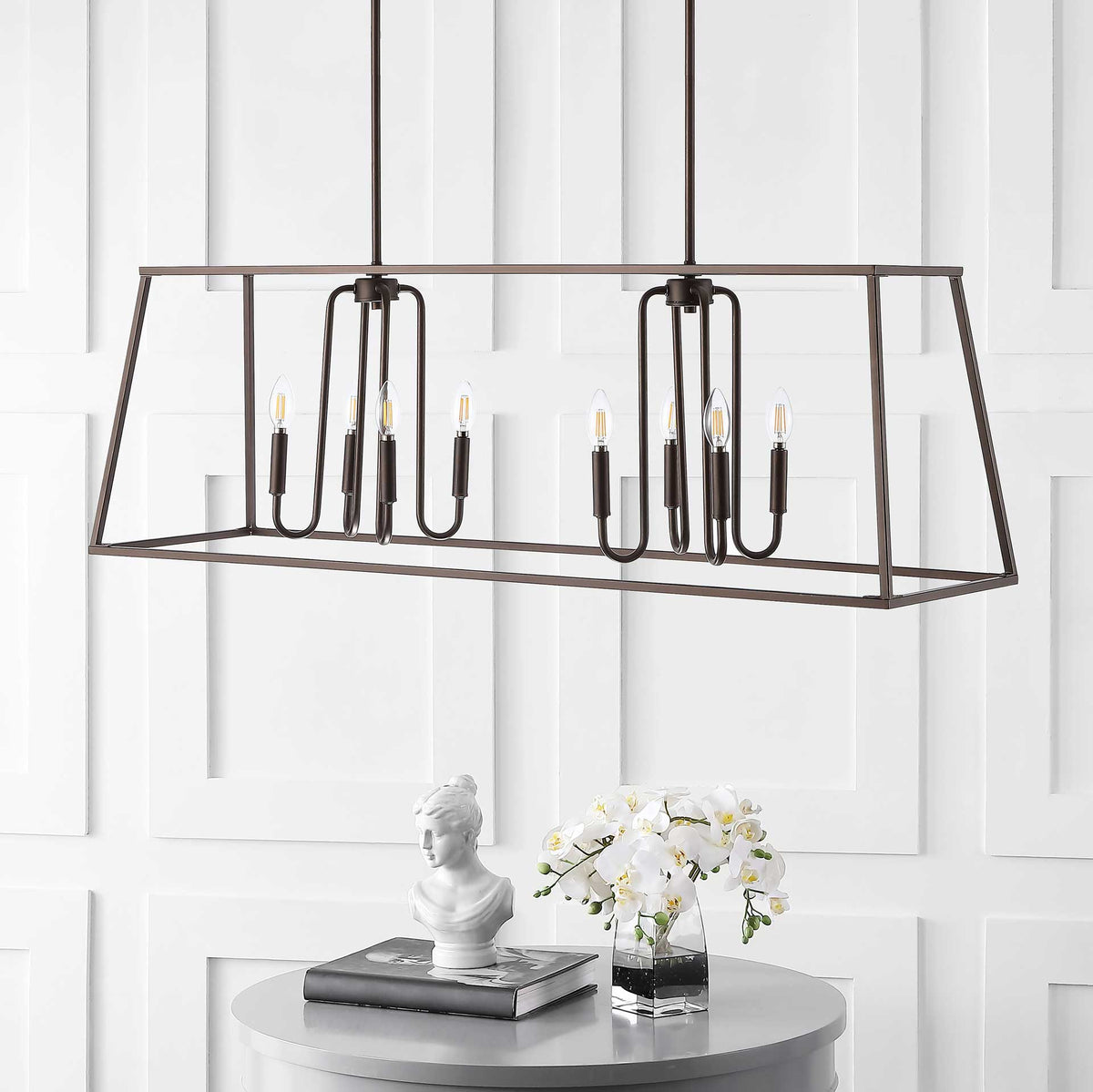 Eight candle-style bulbs sit within a wide, open bronze frame above a round table.
