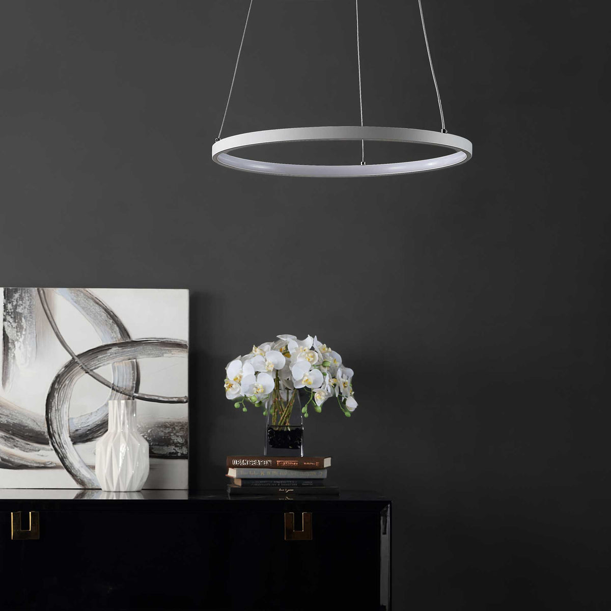 The slender white ring and delicate suspension wires add minimalist style above a dark cabinet.