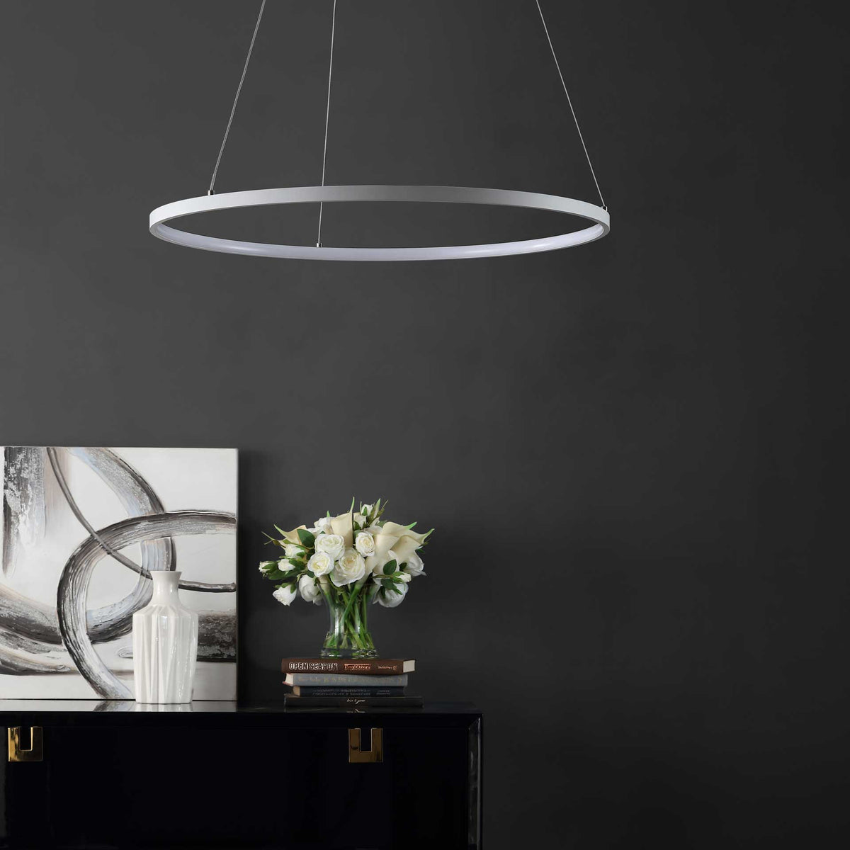 A thin white ring pendant adds an airy, minimalist accent above a dark console and white flowers.