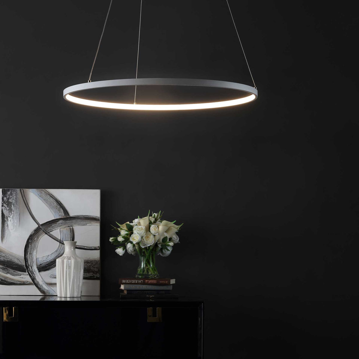Warm LED light outlines a slim white pendant ring above a dark console and floral accents.