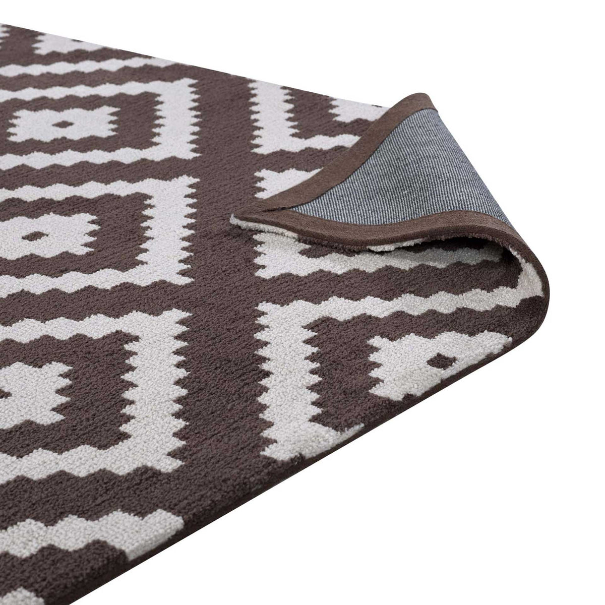 A folded rug edge reveals woven backing beneath the brown and ivory pattern.