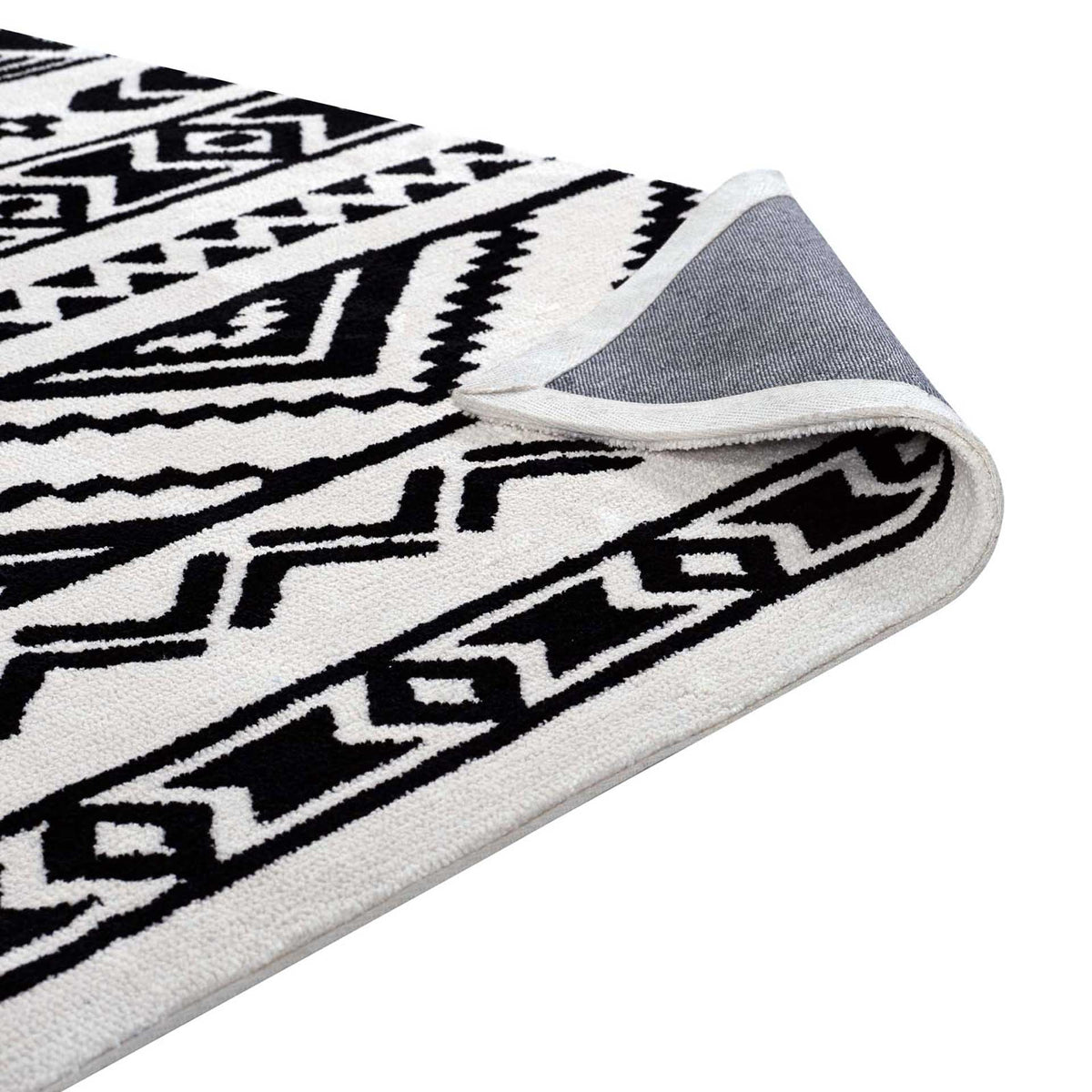 A lifted corner reveals woven gray backing beneath the rug's plush black-and-white pattern.