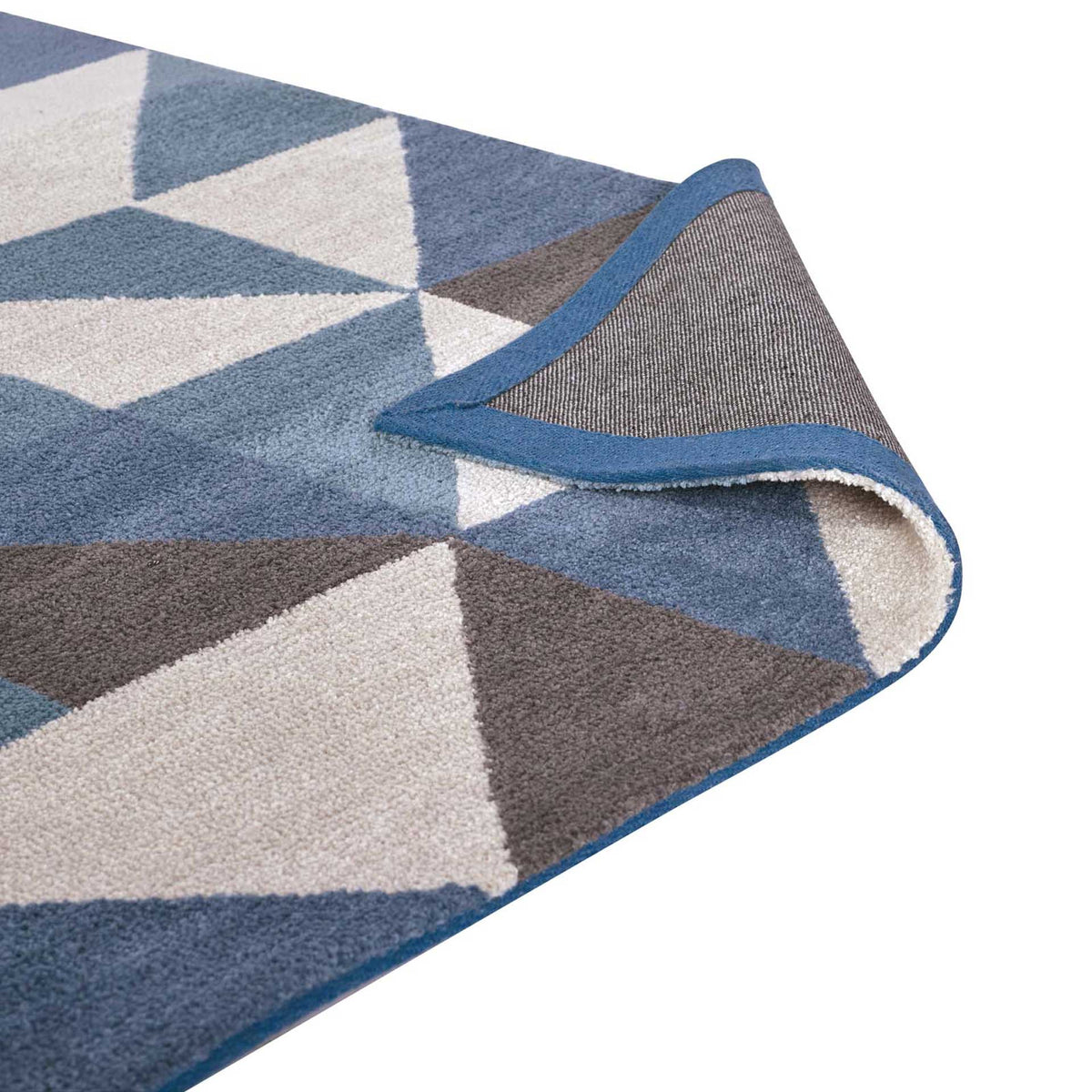 A folded corner reveals woven backing and blue binding beneath the patterned pile