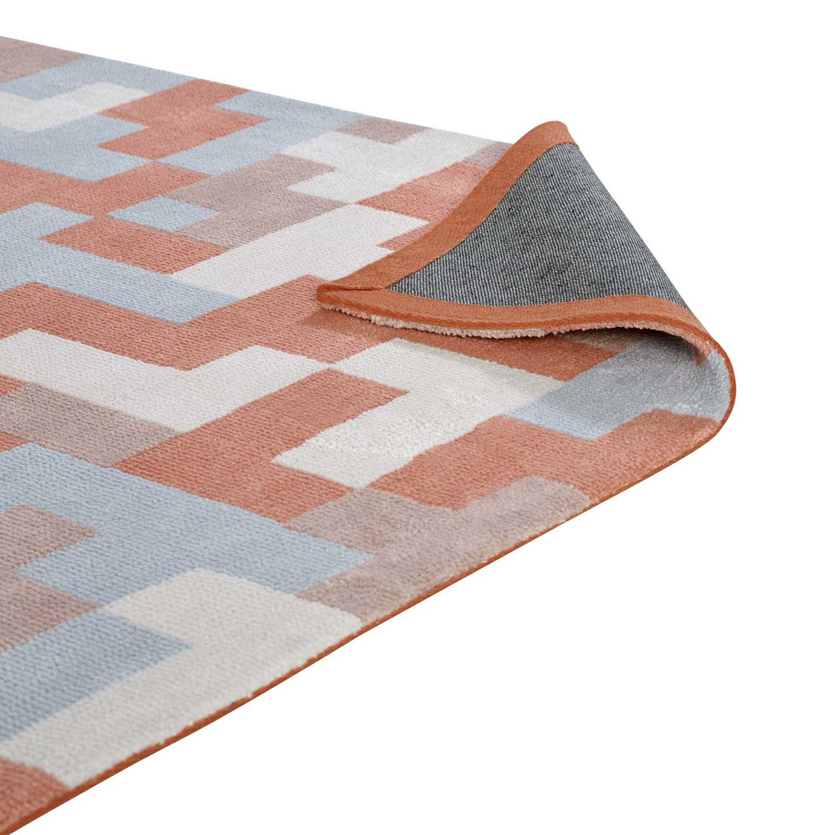A folded edge reveals woven backing beneath the coral and pale blue patterned rug.