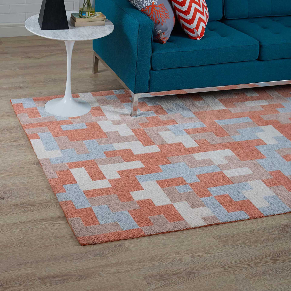 A coral and pale blue geometric rug brings color and comfort beneath a teal sofa.