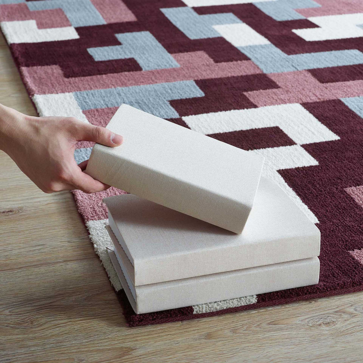 Burgundy and pale blue blocks frame rug pad samples resting on the patterned surface.
