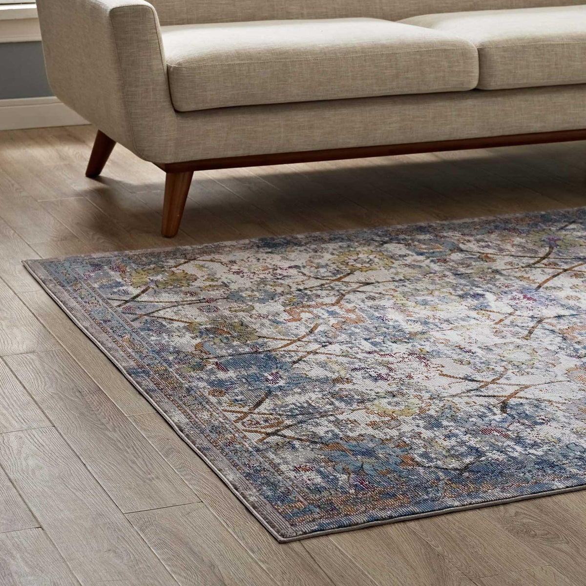 Weathered light blue florals and warm accents soften the floor beside a beige sofa
