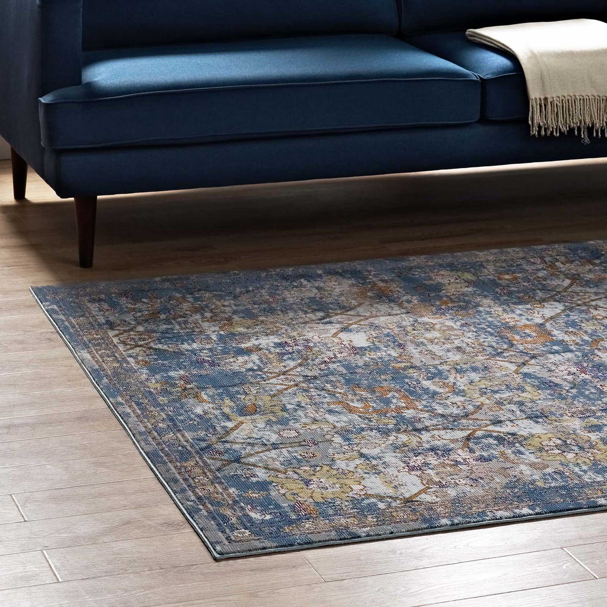 A blue-gray floral rug adds layered color beneath a navy sofa on a wood floor