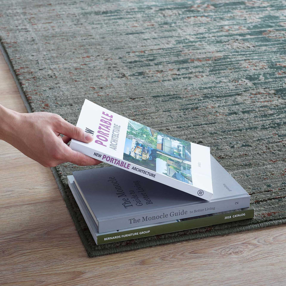 Muted teal and beige threads extend beneath stacked books along the rug's slim bound edge