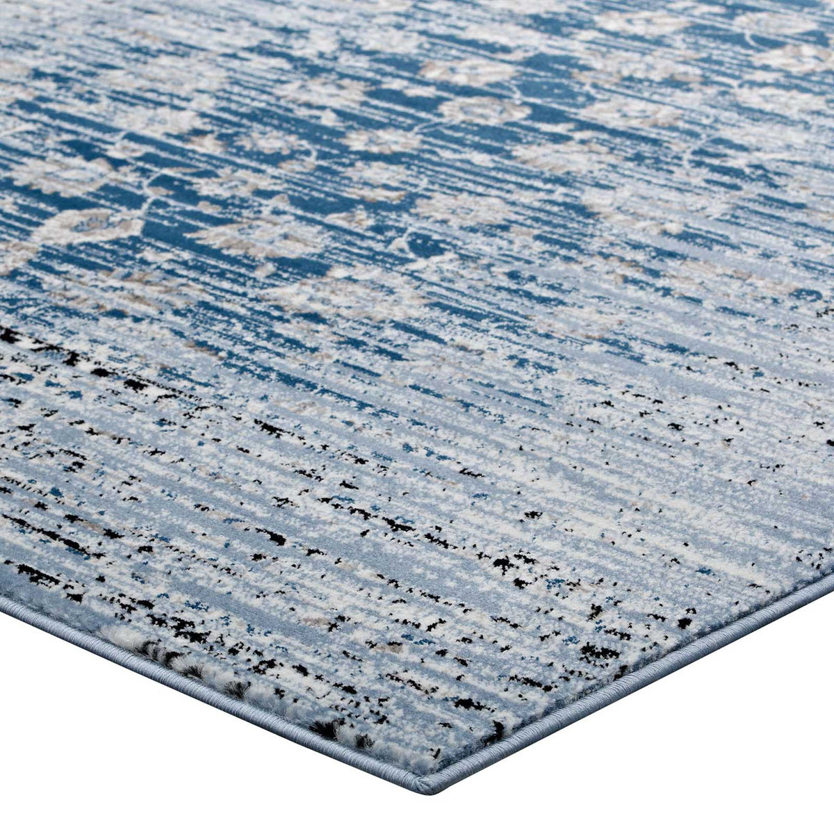 A neatly bound edge frames the rug's low blue pile and softly faded floral pattern.