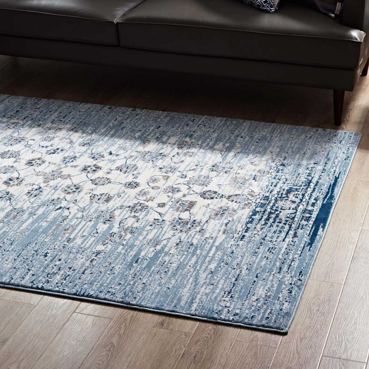 A light ivory floral field and deep blue border brighten the floor beneath a dark sofa.