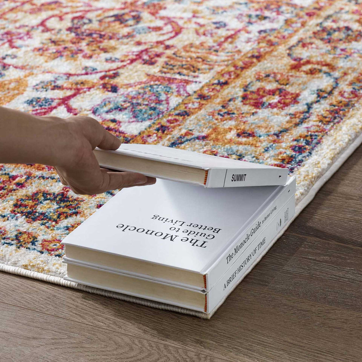 A dense, low-pile floral weave rests neatly beneath stacked books on this ivory rug.