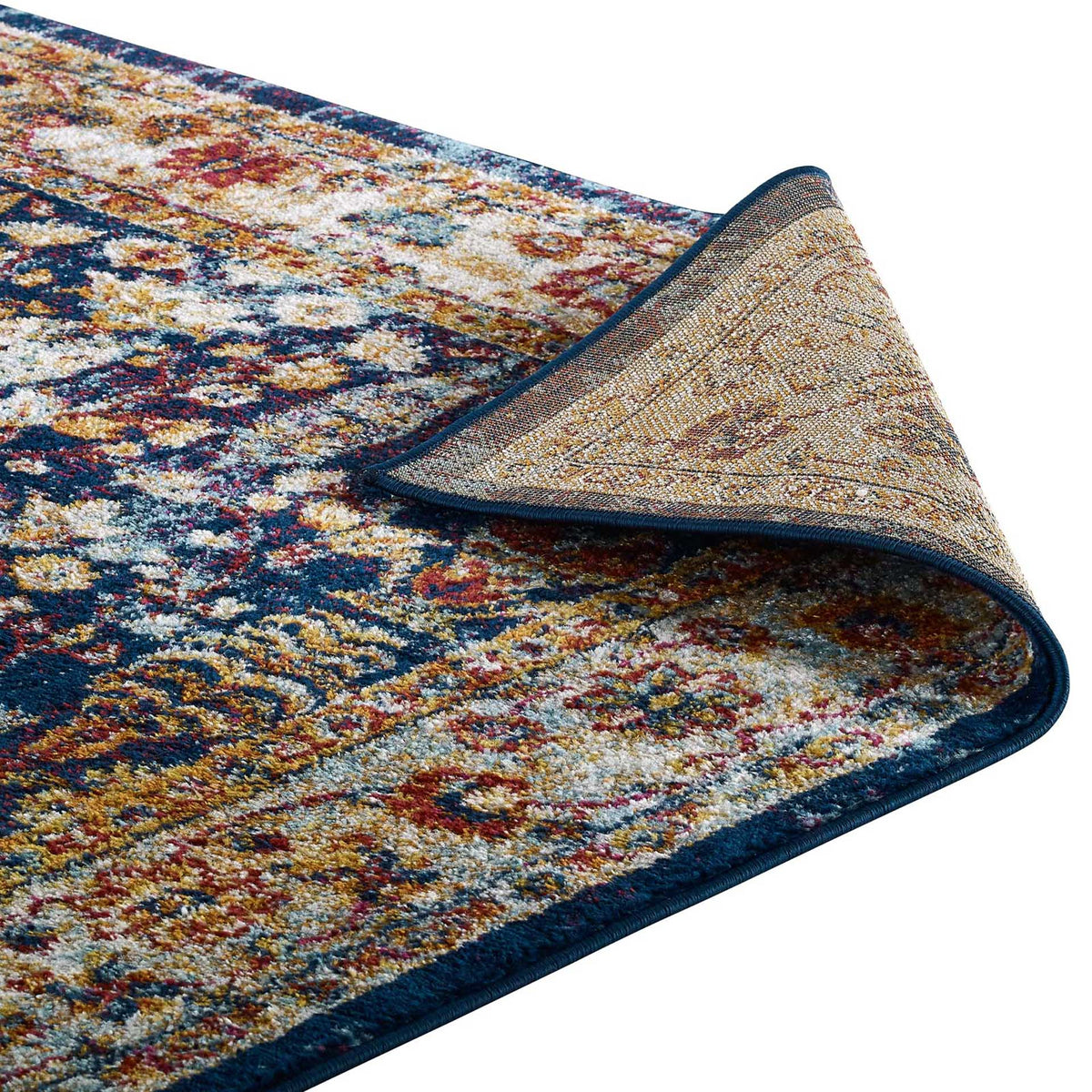 A folded rug edge reveals the textured underside beneath a navy-bound floral surface.