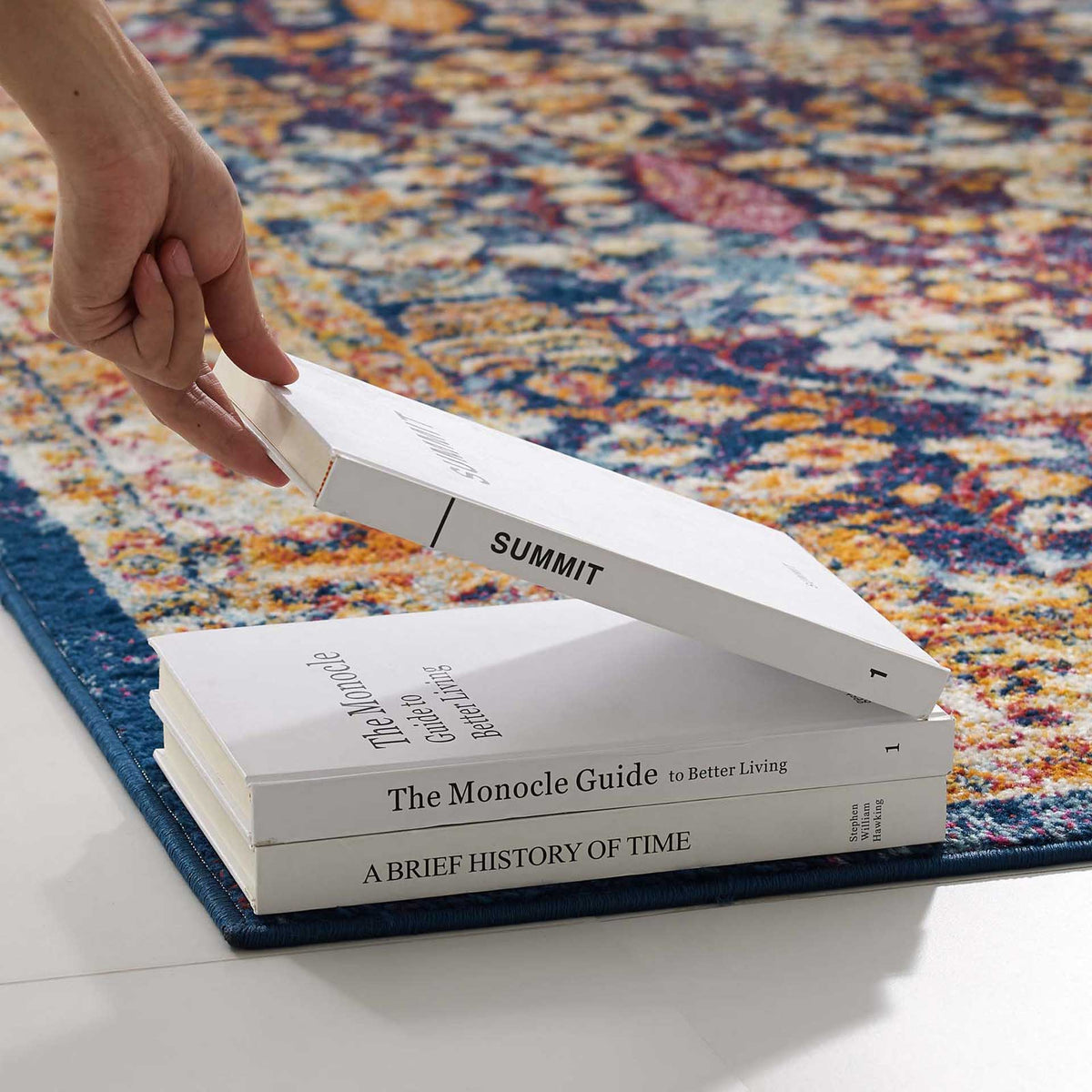 The rug's dense, low pile keeps its lively floral design visible beneath stacked books.
