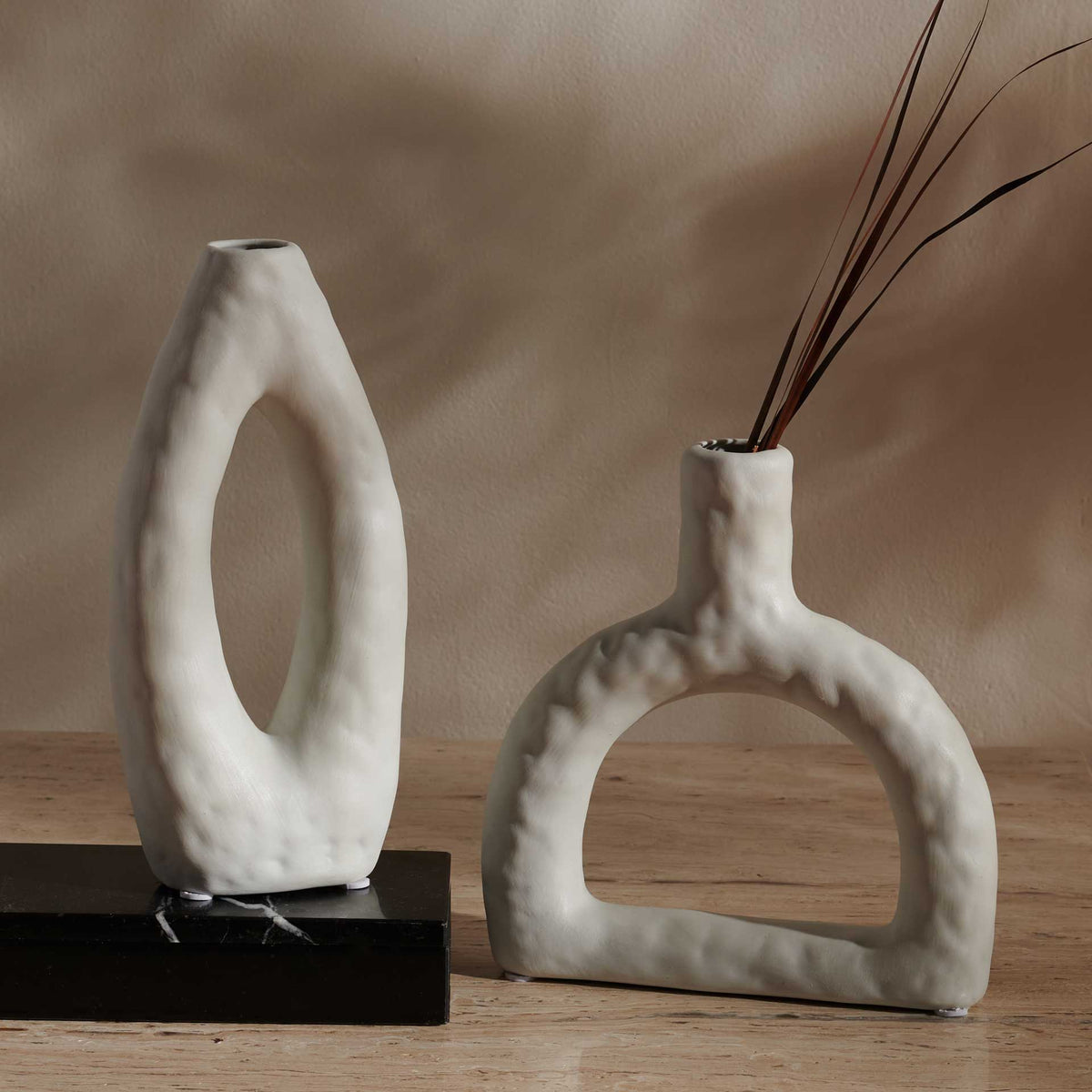 Two sculptural ceramic vases add organic curves to a tabletop, with slender branches in one vessel