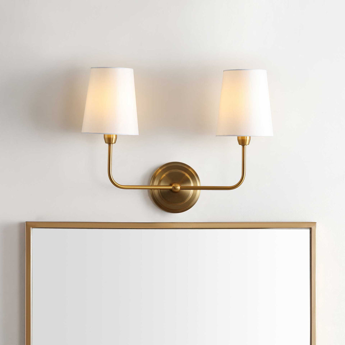 Two softly lit shades cast an inviting glow from a graceful brass-finished sconce.