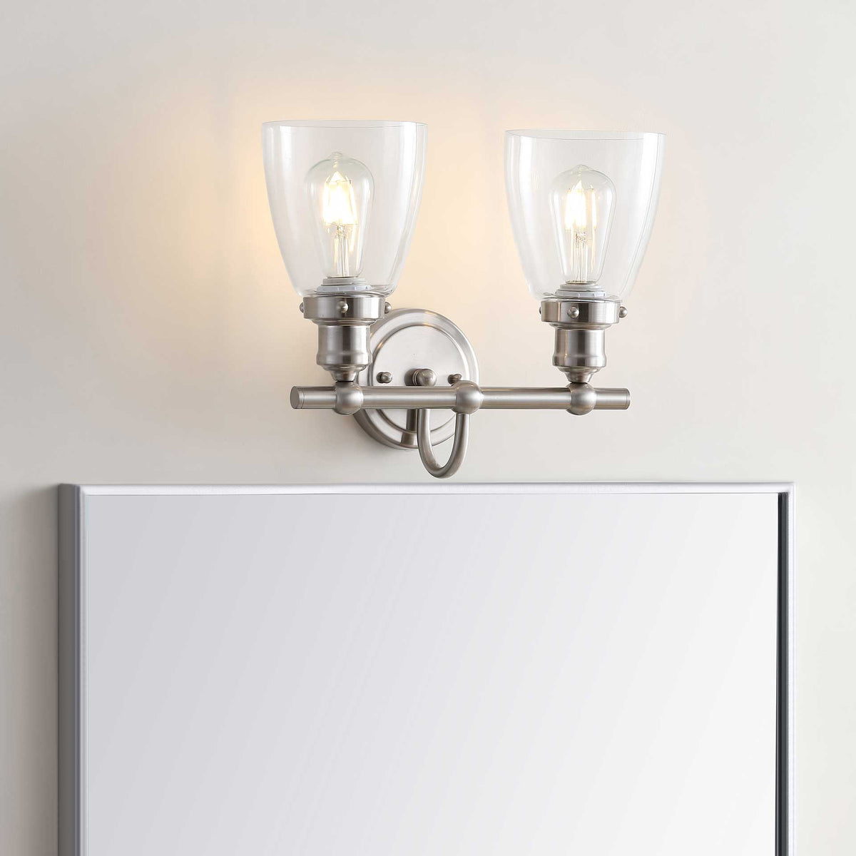 Two upturned glass shades cast a warm glow above a bathroom mirror