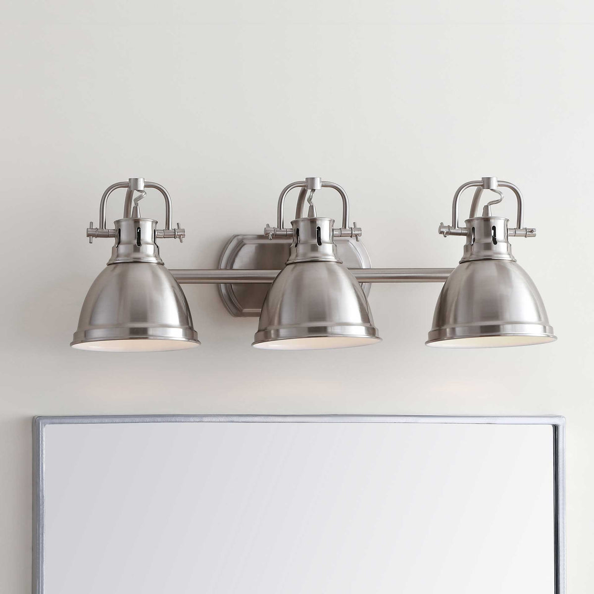 Three downward-facing metal shades cast a warm glow across the vanity.