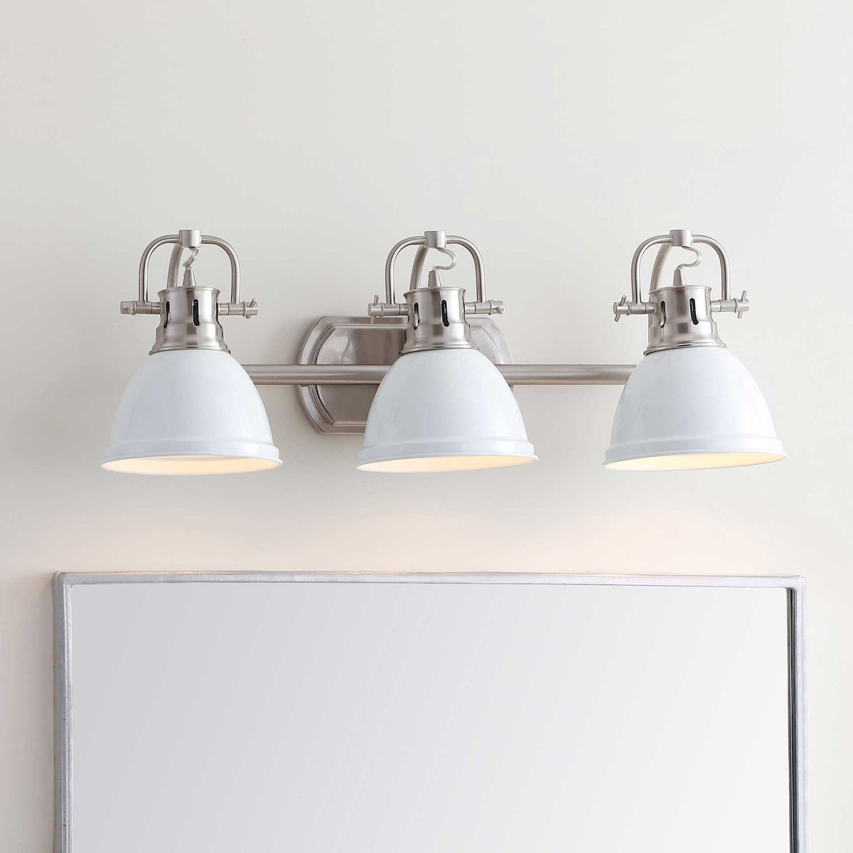 White shades cast a warm glow above the vanity from a three-light sconce.