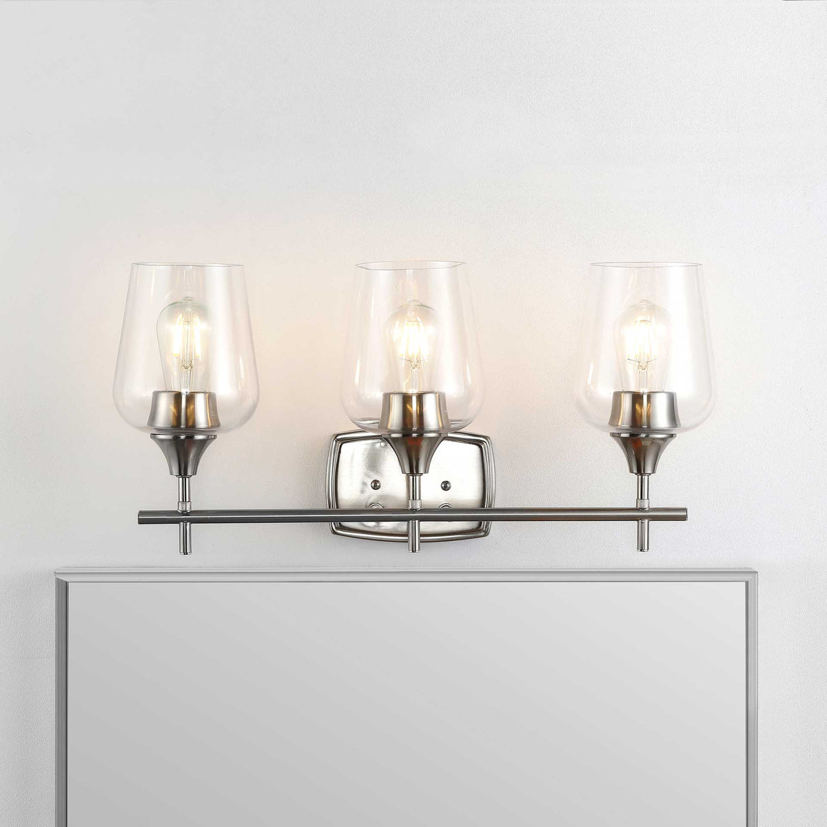 Warm light from three filament bulbs shines through clear glass shades above a nickel-finished bar.