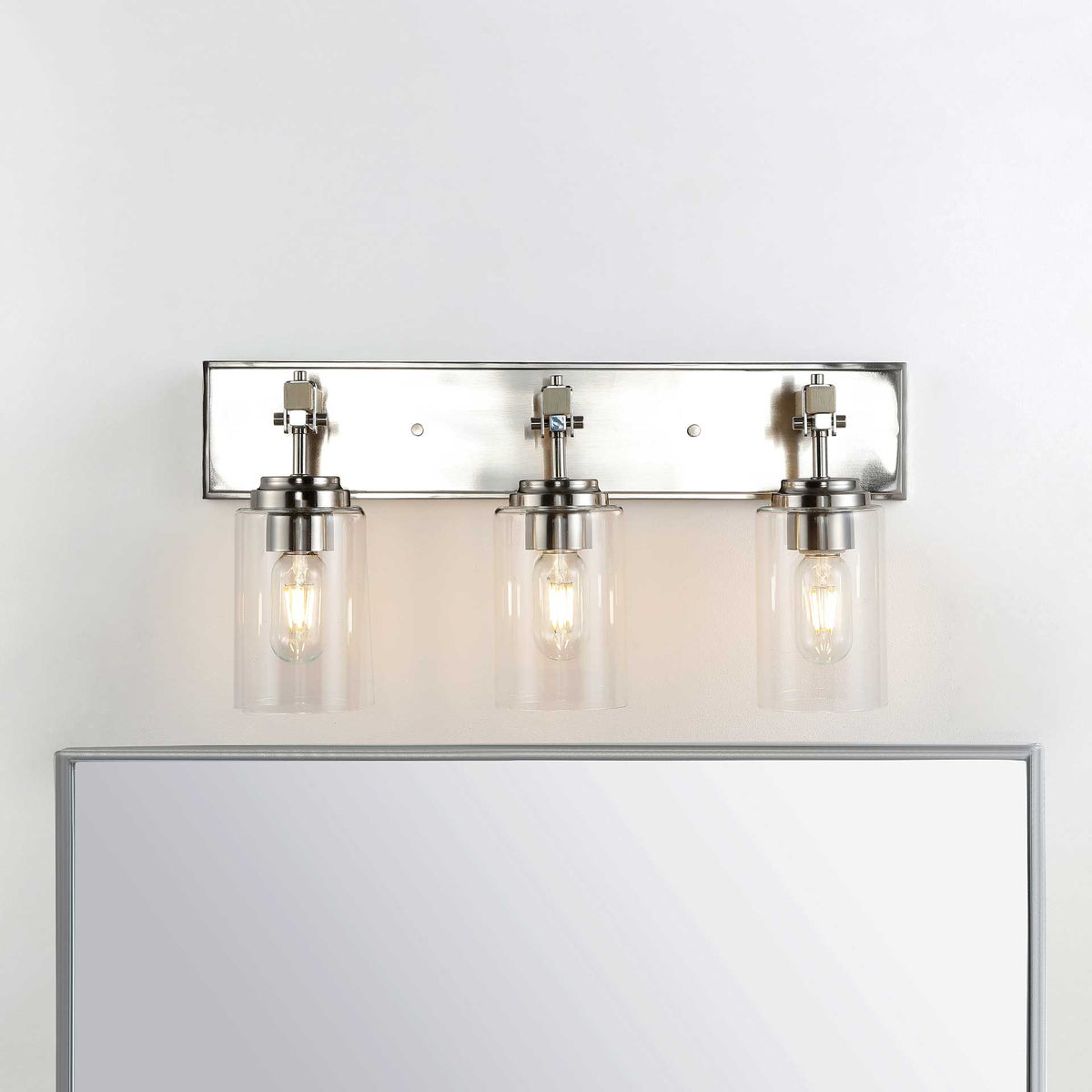 Three illuminated glass shades bring a warm glow to the space above a mirror.