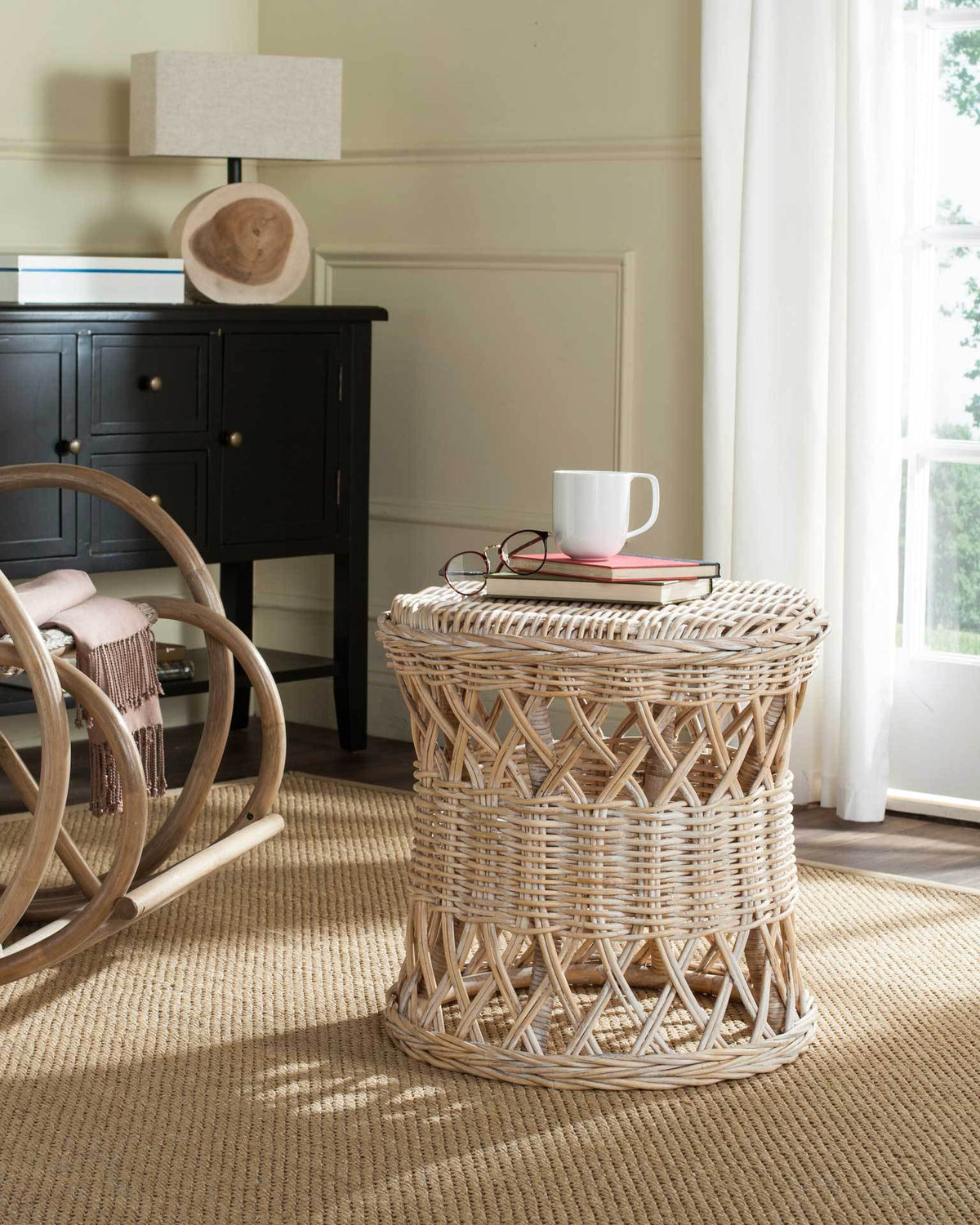Natural wicker table holds books and a mug on its woven top above an open rattan base