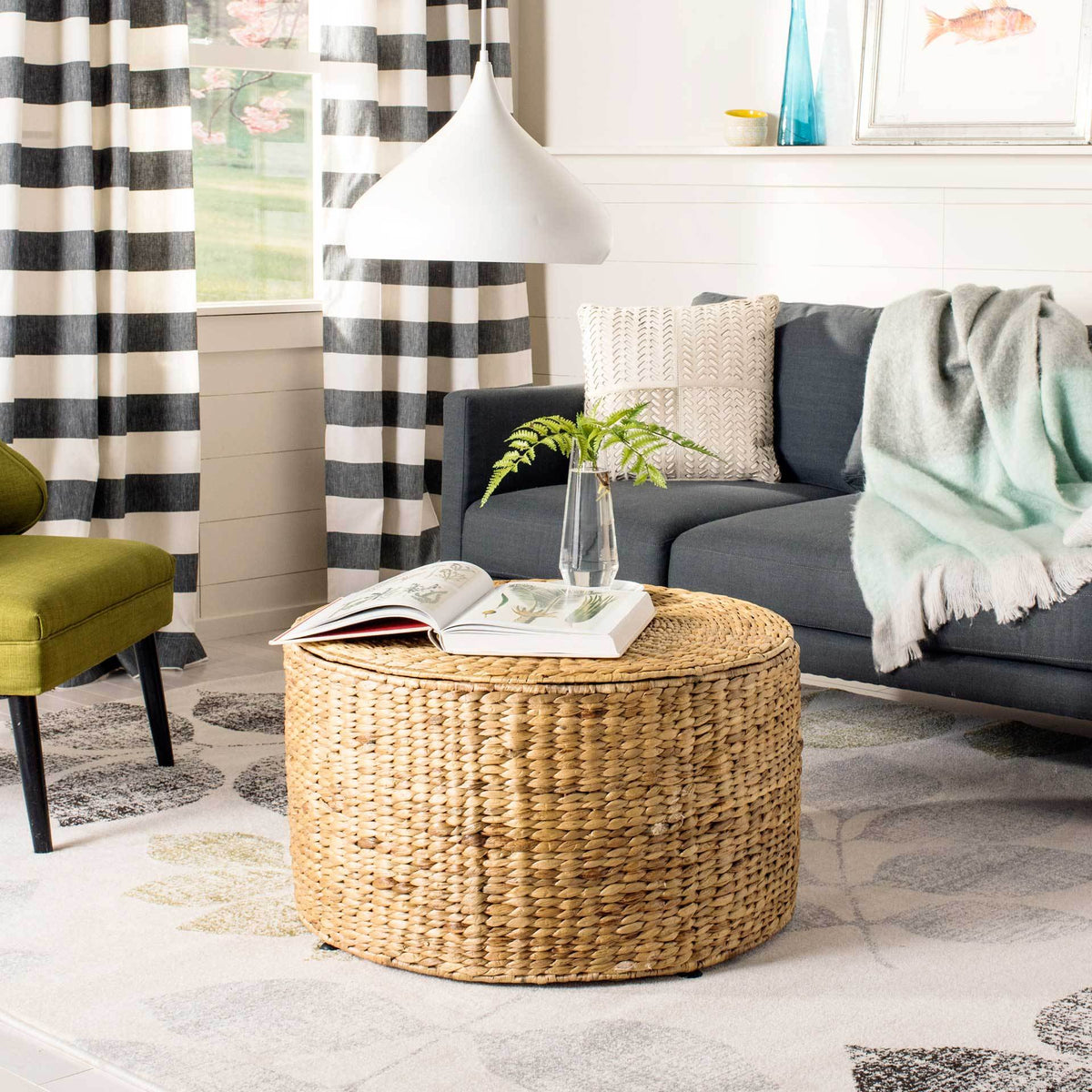 A honey-toned wicker coffee table adds warm texture to a living room beneath books and a clear vase.